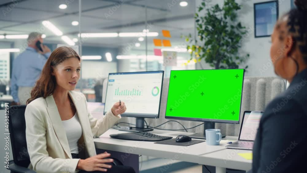 Poster Two Female Colleagues Fondly Talk to Each Other, Laugh and Smile while Working on Computers with Green Screen Mock Up Display in Modern Business Office. Manager and Employee Discuss a Fun Project.