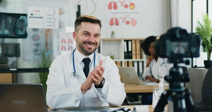 Likable smiling satisfied high-skilled bearded doctor clapping hands after ending his medical video chat via camera with online audience ,slow motion