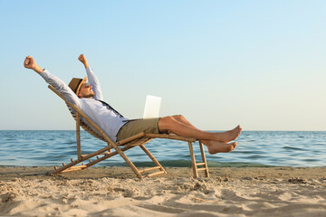 Happy man with laptop resting on deckchair near sea. Business trip - obrazy, fototapety, plakaty