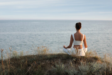 Fototapeta na wymiar Woman meditating near sea, back view. Space for text