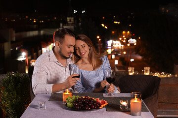 Romantic couple with glasses of red wine on cafe terrace at night