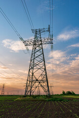 high voltage lines and power pylons in a green agricultural field against a saturated sunset sky