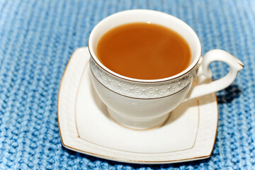 White cup and saucer with coffee with milk on the background of a knitted sweater.