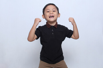 The Asian boy who is wearing a black t-shirt is looking forward while clenching his fists with a happy expression. White background. 