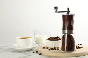 Manual coffee grinder with powder, beans and cup of drink on white marble table