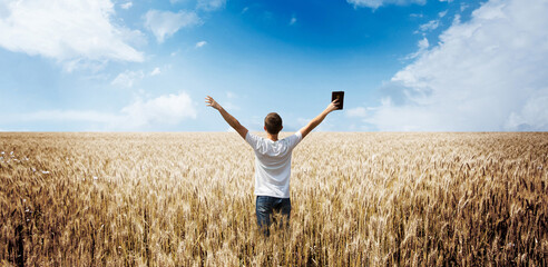 man holding up Bible in a wheat field - 453818582