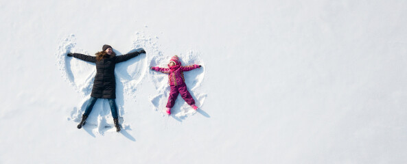 Child girl and mother playing and making a snow angel in the snow. Top flat overhead view - 453818711