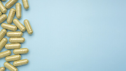 Flat lay of Andrographis paniculata capsules isolated on light blue background. Space for text. Herbal, medicine, and healthcare concept