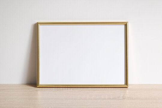 Pusta złota ramka na zdjęcia na komodzie oparta o ścianę