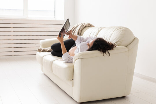 Hispanic pregnant woman using tablet computer while lying on sofa at home. Pregnancy and information for parenthood concept.
