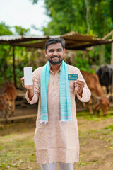 Young indian farmer showing debit or credit card at his farm