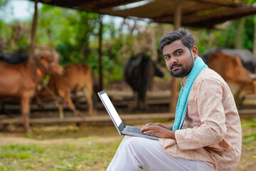 Young indian farmer using laptop at his cattle farm