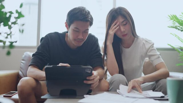 asian marry couple checking and calculate financial billing together on sofa involved in financial paperwork, paying taxes online using e-banking laptop at living room home 