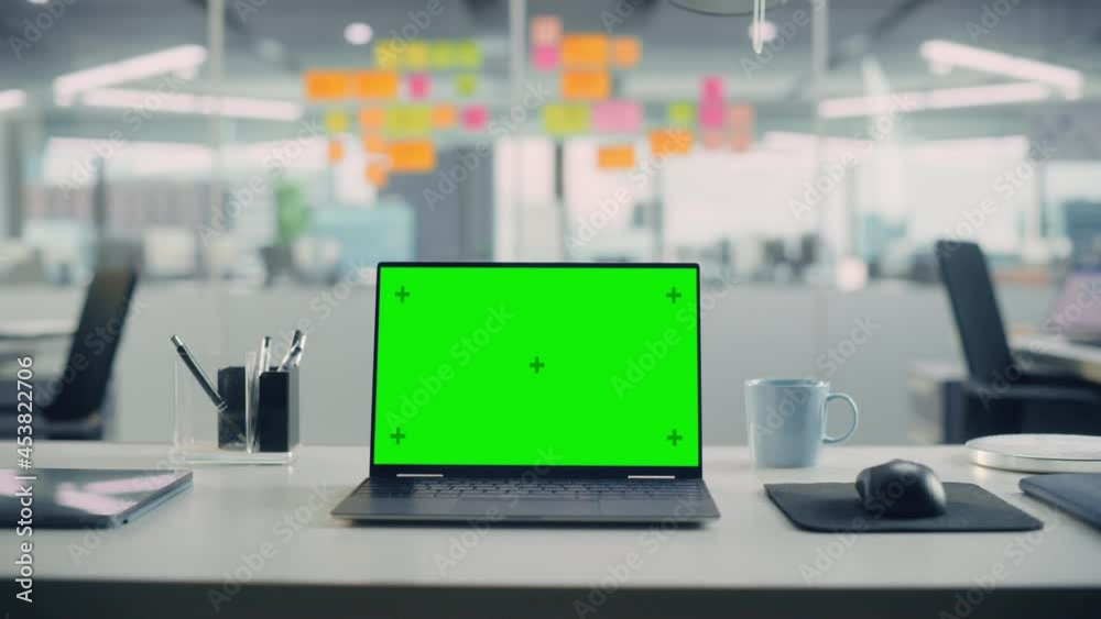Poster Laptop Computer with Mock Up Green Screen Chroma Key Display Standing on the Desk in the Modern Creative Office. In the Background Glass Wall with Colorful Planning Notes. Zoom in Shot.