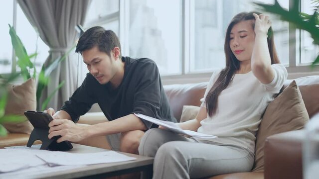 asian marry couple checking and calculate financial billing together on sofa involved in financial paperwork, paying taxes online using e-banking laptop at living room home 