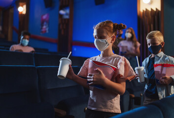 Happy small children with popcorn walking in the cinema, coronavirus concept.