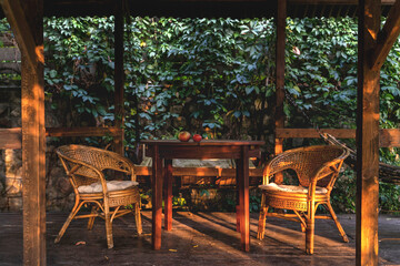 Cozy wooden gazebo with a round table and rattan chairs during sunset