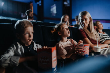 Mother with happy small children in the cinema, watching film.