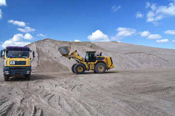 Wheel loader loads a truck with sand in a gravel pit