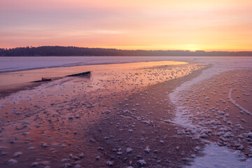 Winter landscape of frozen lake at sunset in warm purple tones.