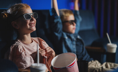 Small children with 3d glasses and popcorn in the cinema, watching film.