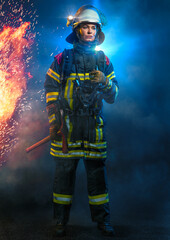 Feuerwehrfrau stehend in voller Ausrüstung vor Flammen und blauem Licht - obrazy, fototapety, plakaty