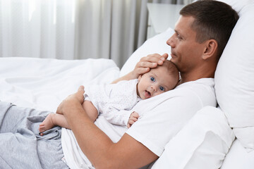 Happy father holding his cute baby on bed at home