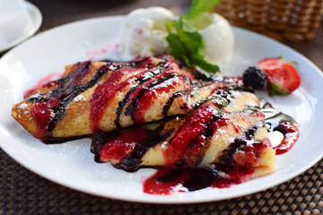 Crepes stuffed with fruit and covered with chocolate and berry syrups. Served with ice cream balls and strawberries. Thin pancakes, blini. Sweet dessert.