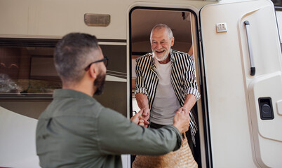 Mature man with senior father unpacking by car outdoors, caravan holiday trip.