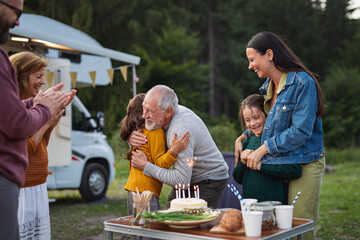 Multi-generation family celebrating birthday outdoors at campsite, caravan holiday trip.