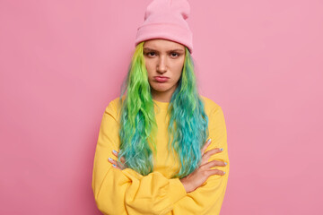 Studio shot of offended displeased hipster girl with long dyed hair keeps arms folded doesnt speak...