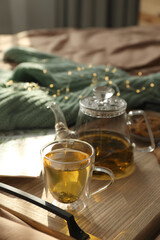 Wooden tray with freshly brewed tea on bed in room. Cozy home atmosphere