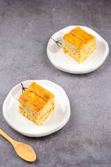 Close up square cut of homemade sweet and solf carrot cake on white plate with wooden spoon on table. Delicious and healthy bakery.