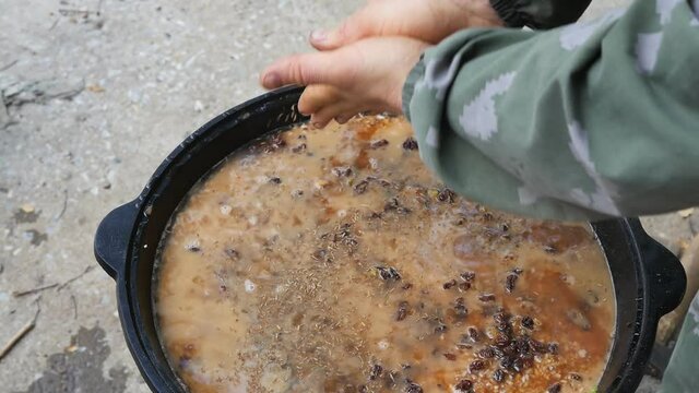 a man cook rubs cumin with his palms and pours seasoning into a large cauldron with hot pilaf. Cooking the national Uzbek dish in the open air. Slow motion, close-up.