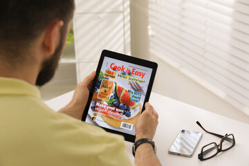 Man reading online magazine on tablet at white table, closeup