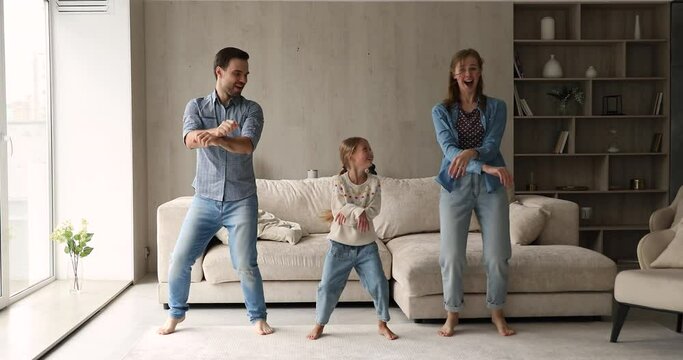 Happy family with daughter dance barefoot in living room making funny Gangnam style movements feels overjoyed having fun together on weekend at home. Hobby, tenant, celebrate moving day to new house