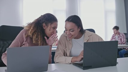 Cheerful students talking in library, whispering secrets, friendly communication
