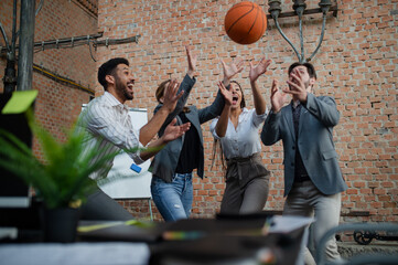 Group of cheerful young businesspeople playing basketball in office, taking a break concept.