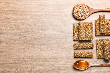 Delicious sweet kozinaki bars, honey and sunflower seeds on wooden table, flat lay. Space for text