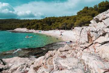 Fototapeta na wymiar Focus on the rock on the Srebrna Beach in Croatia, Vis island in the summer of 2021. Beach filled with people in the background blurred
