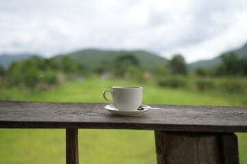 Hot coffee cup  on the wooden table and the plantations background with copy space for your text