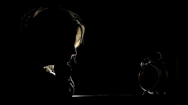 Woman in the dark looking time passing on clock, insomnia