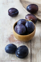 Bowl with ripe plums on wooden table