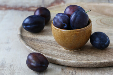 Bowl with ripe plums on wooden table