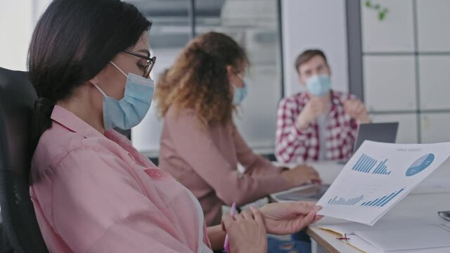 Corporate managers in protective masks discussing reports in office, covid-19