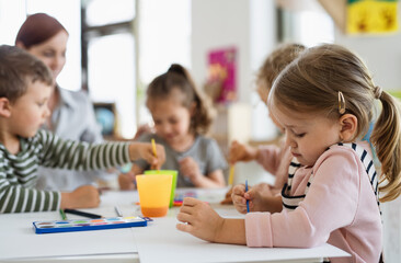 Group of small nursery school children with teacher indoors in classroom, painting.