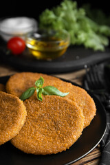 Delicious fried breaded cutlets with basil on wooden table, closeup