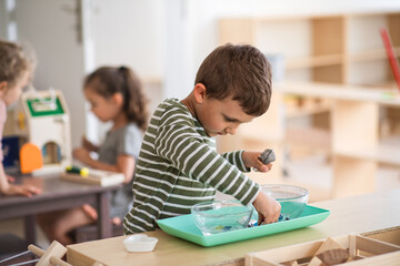 Small nursery school boy playing indoors in classroom, montessori learning.