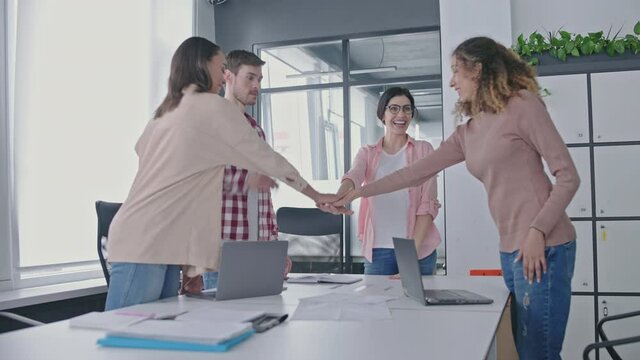 Happy sales managers joining hands in office, team building, work motivation