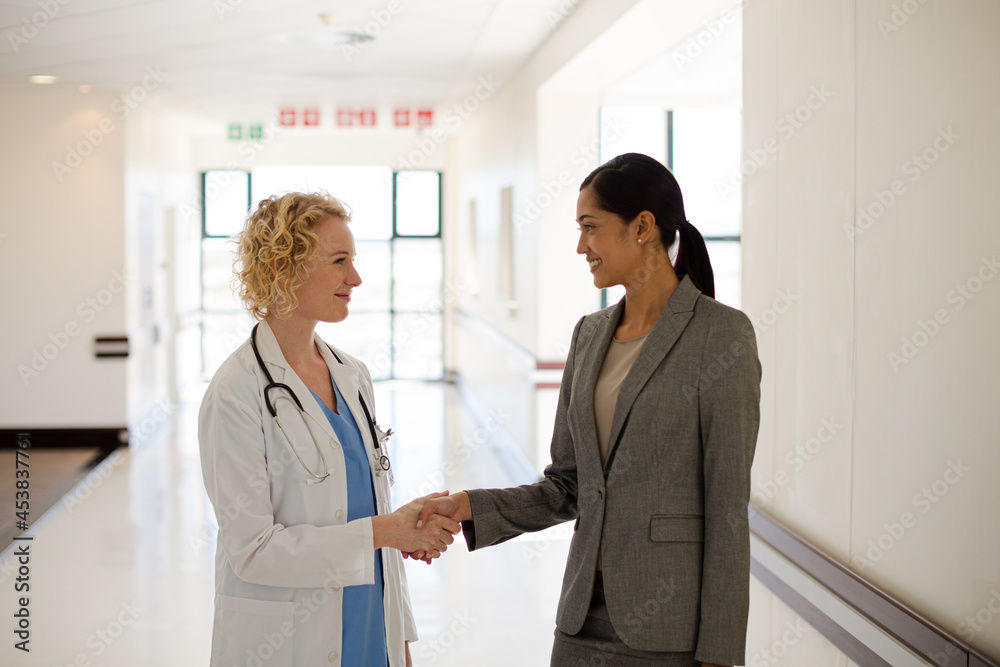 Wall mural doctor and businesswoman handshaking in hospital corridor